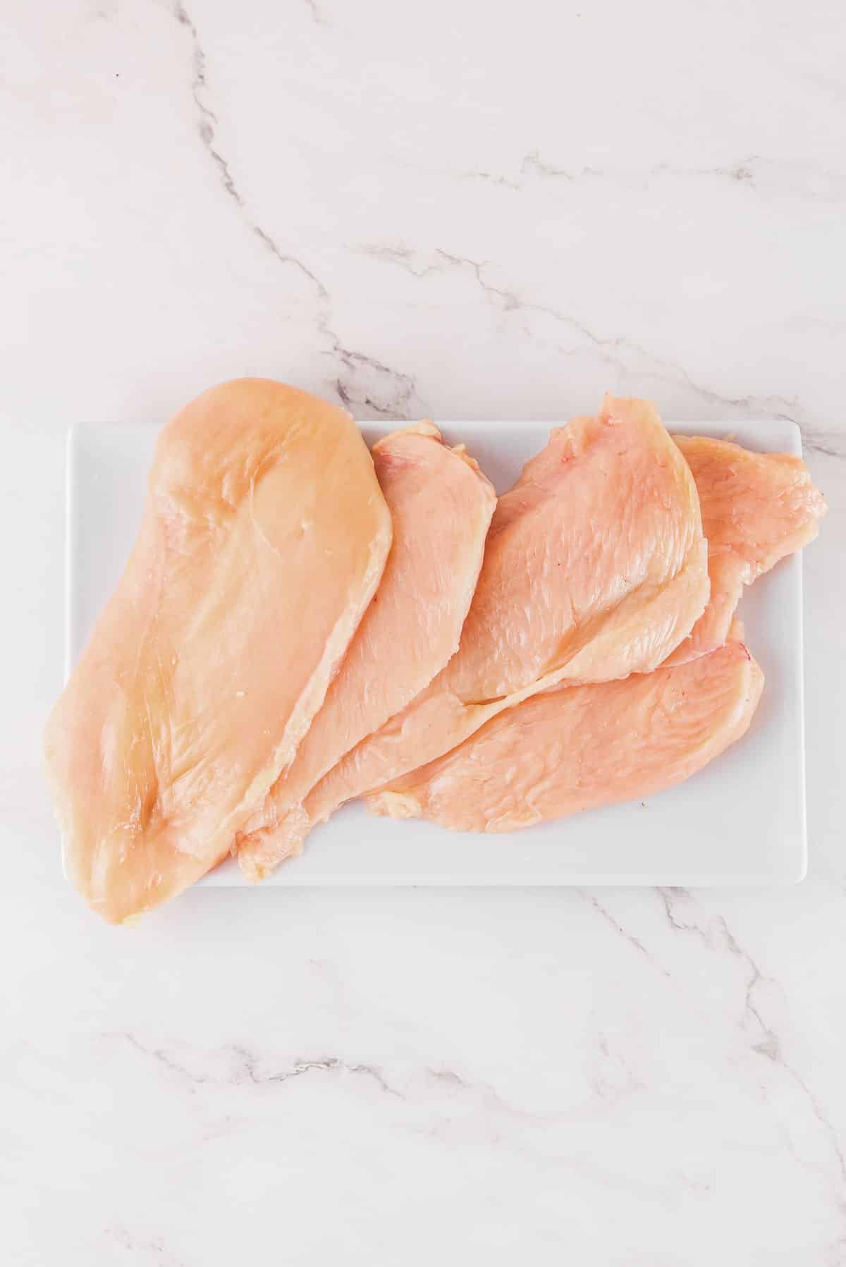 four thinly sliced chicken breasts on a white cutting board.