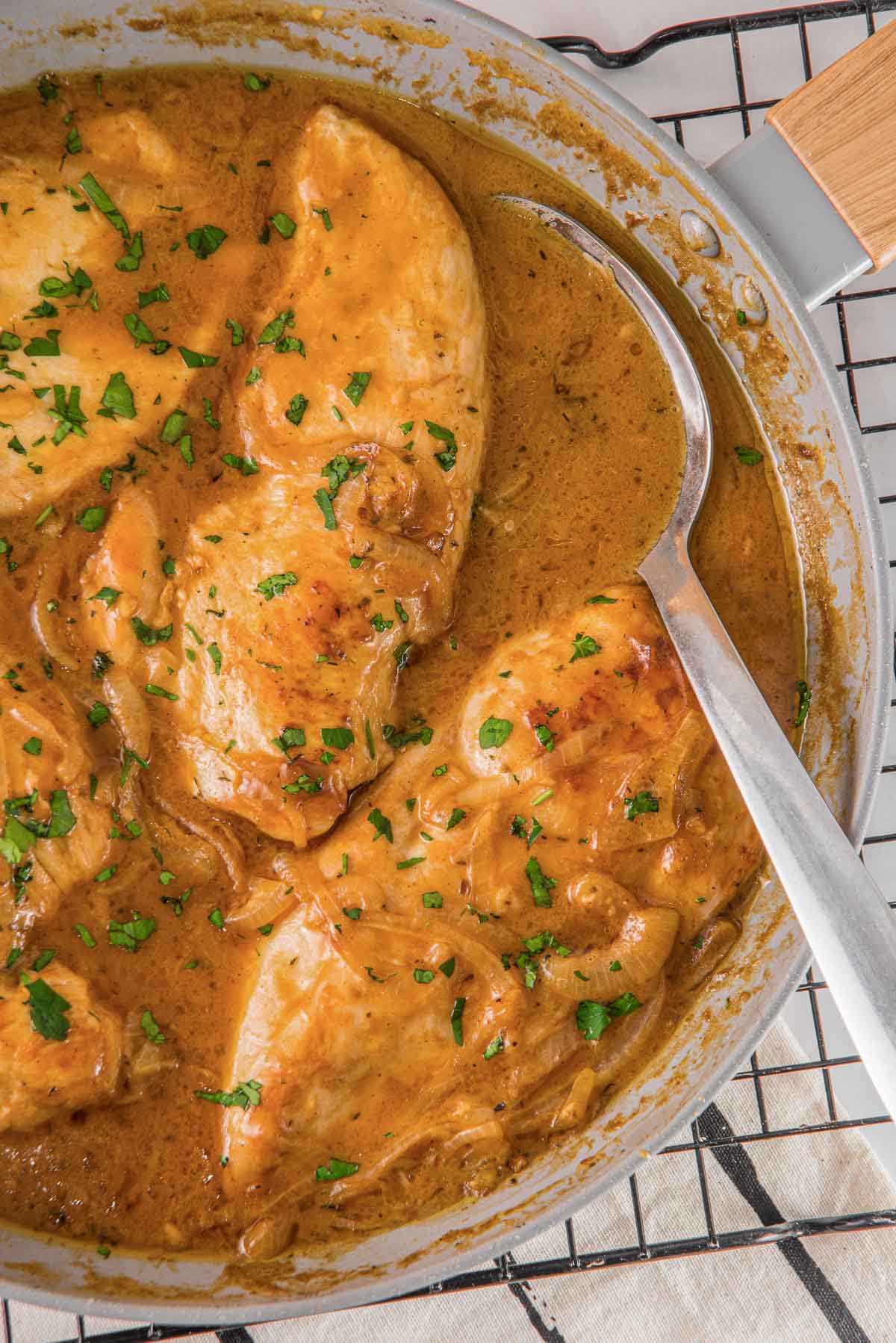 Chicken in a sauce with fresh parsley in a pan with a spoon.