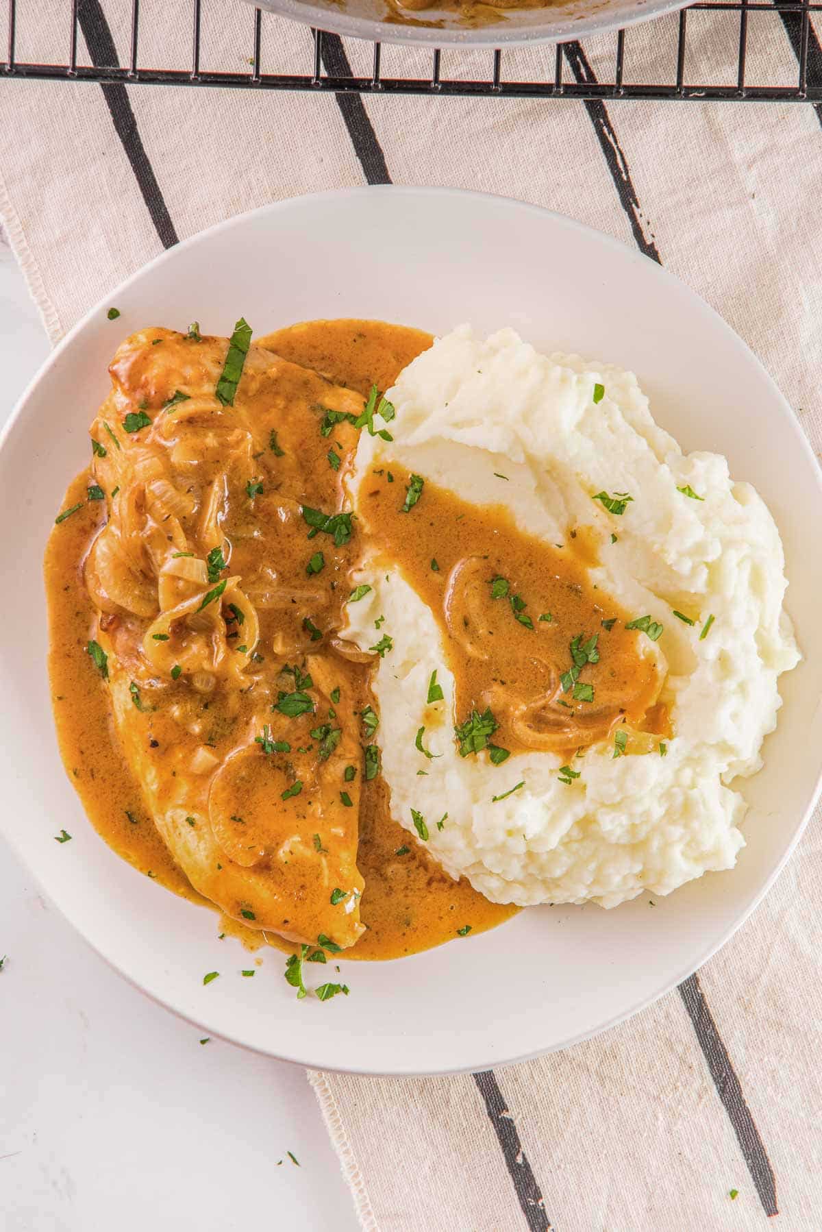 A white plate of smothered chicken recipe with onions, gravy and mashed potatoes.