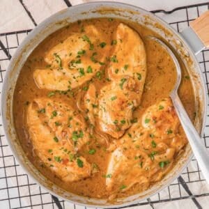 easy smothered chicken recipe in a creamy sauce in a skillet with a spoon.