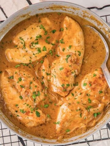 easy smothered chicken recipe in a creamy sauce in a skillet with a spoon.