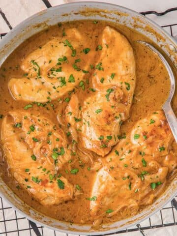 easy smothered chicken recipe in a creamy sauce in a skillet with a spoon.