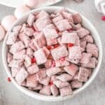 white bowl full of strawberry muddy buddy recipe with red candy hearts in it.