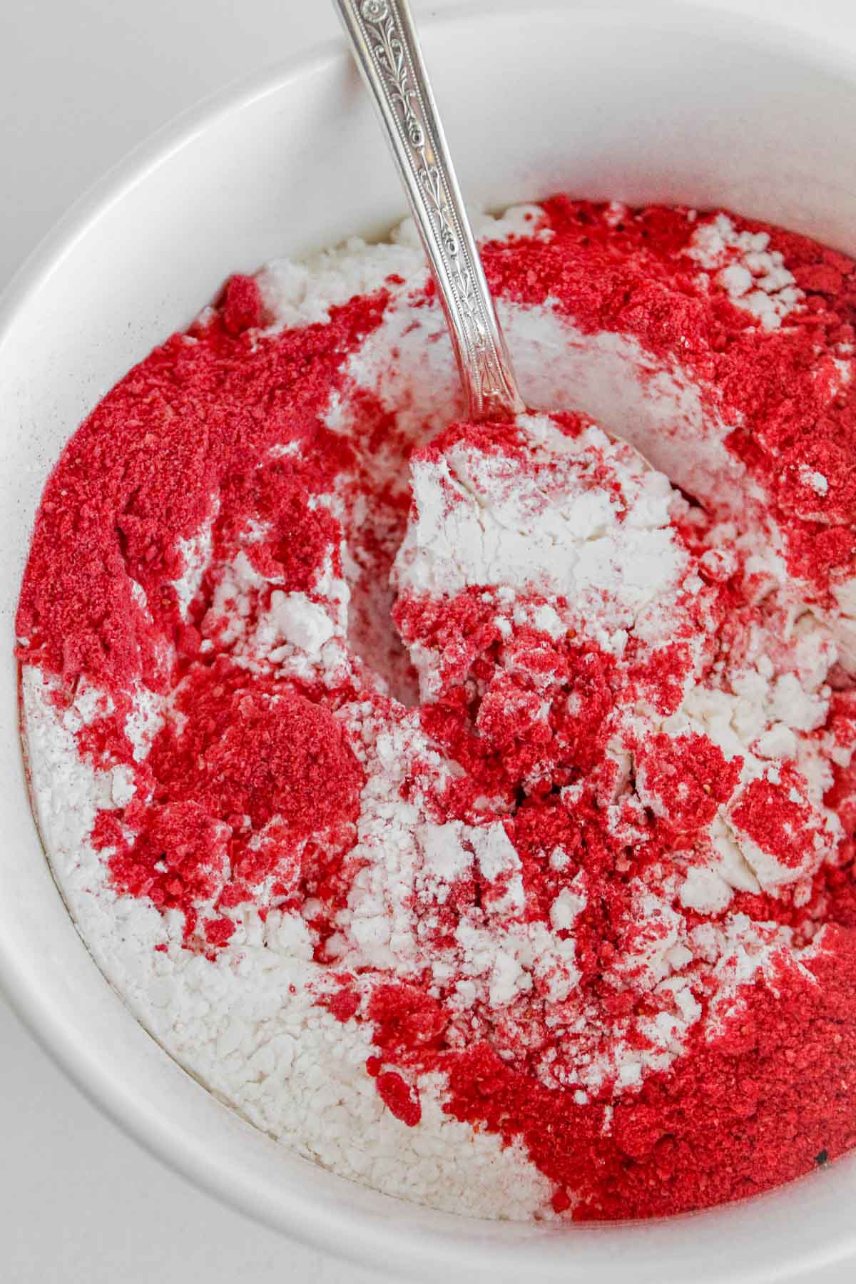 A white bowl filled with powdered sugar and crushed freeze dried strawberries.