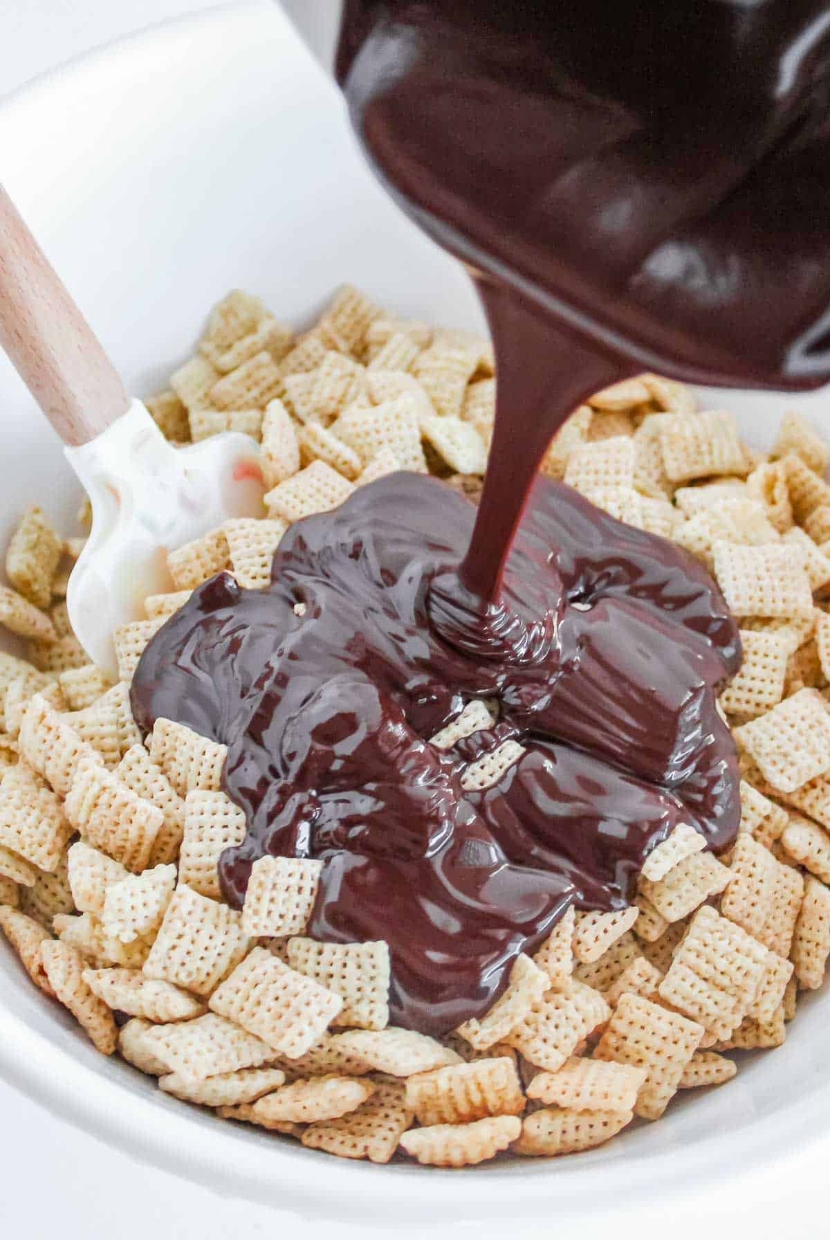 A person pouring melted chocolate over a bowl of Chex cereal.