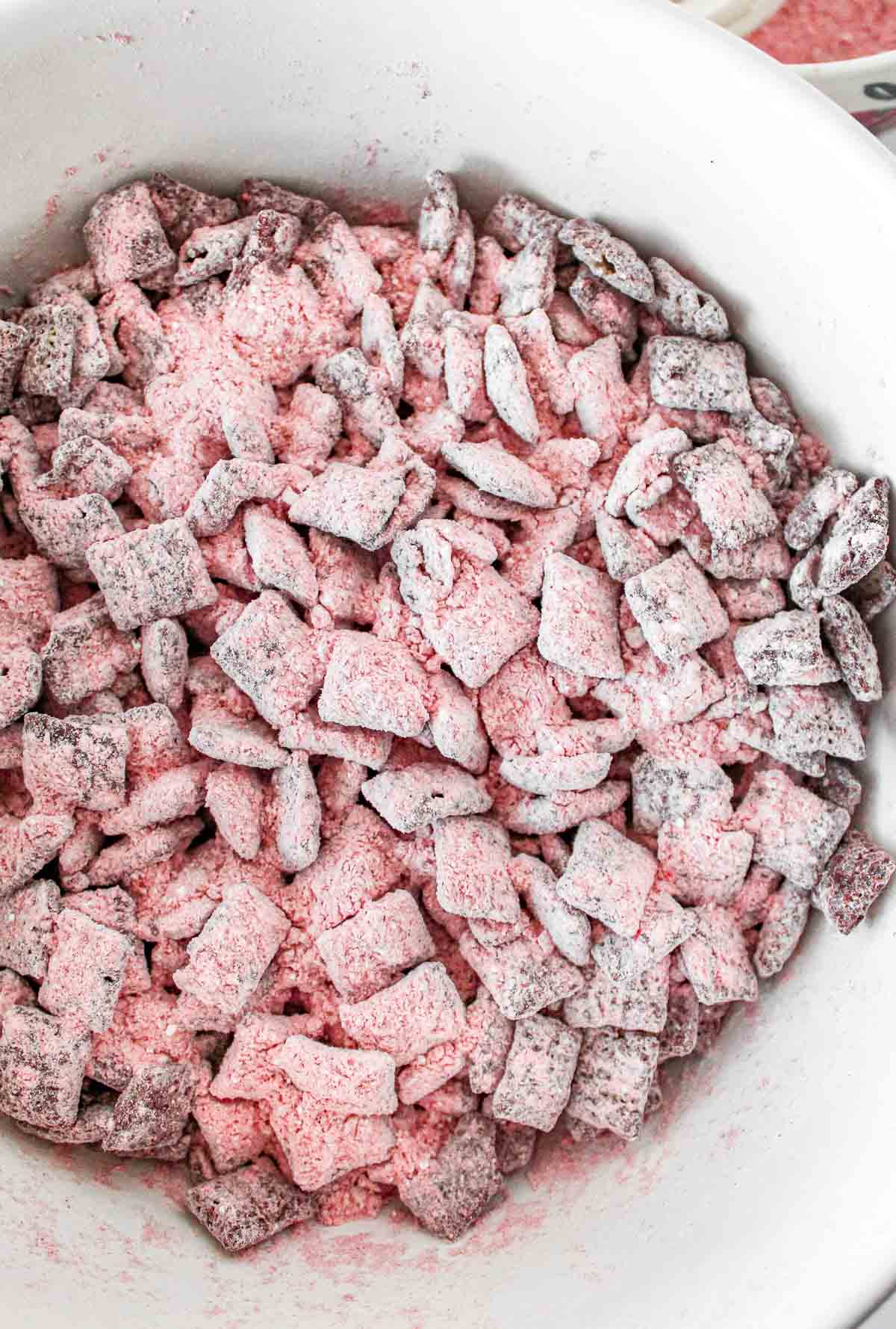 A bowl full of chocolate covered chex mix with pink strawberry flavored powdered sugar.