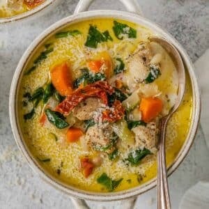 A bowl of easy tuscan chicken soup with carrots, spinach and sun dried tomatoes and a spoon.