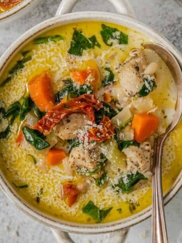 A bowl of easy tuscan chicken soup with carrots, spinach and sun dried tomatoes and a spoon.