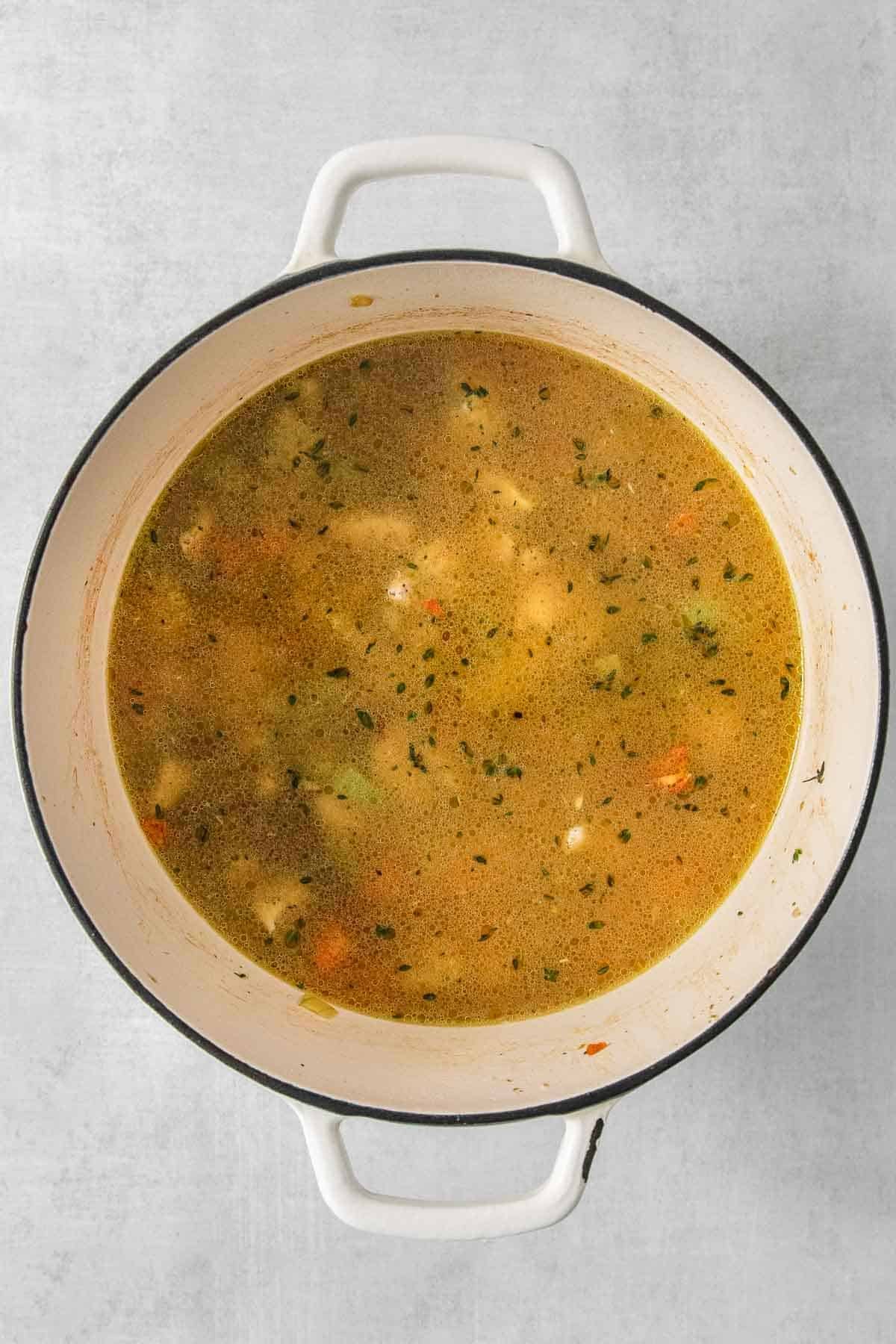 Chicken soup in a white pot on a grey background.