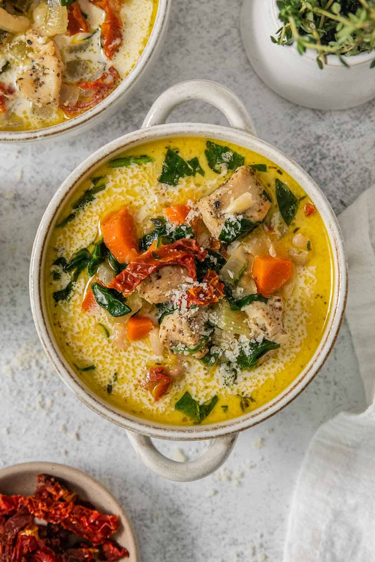 A bowl of easy tuscan chicken soup with carrots, spinach and sun dried tomatoes and a spoon on a table.