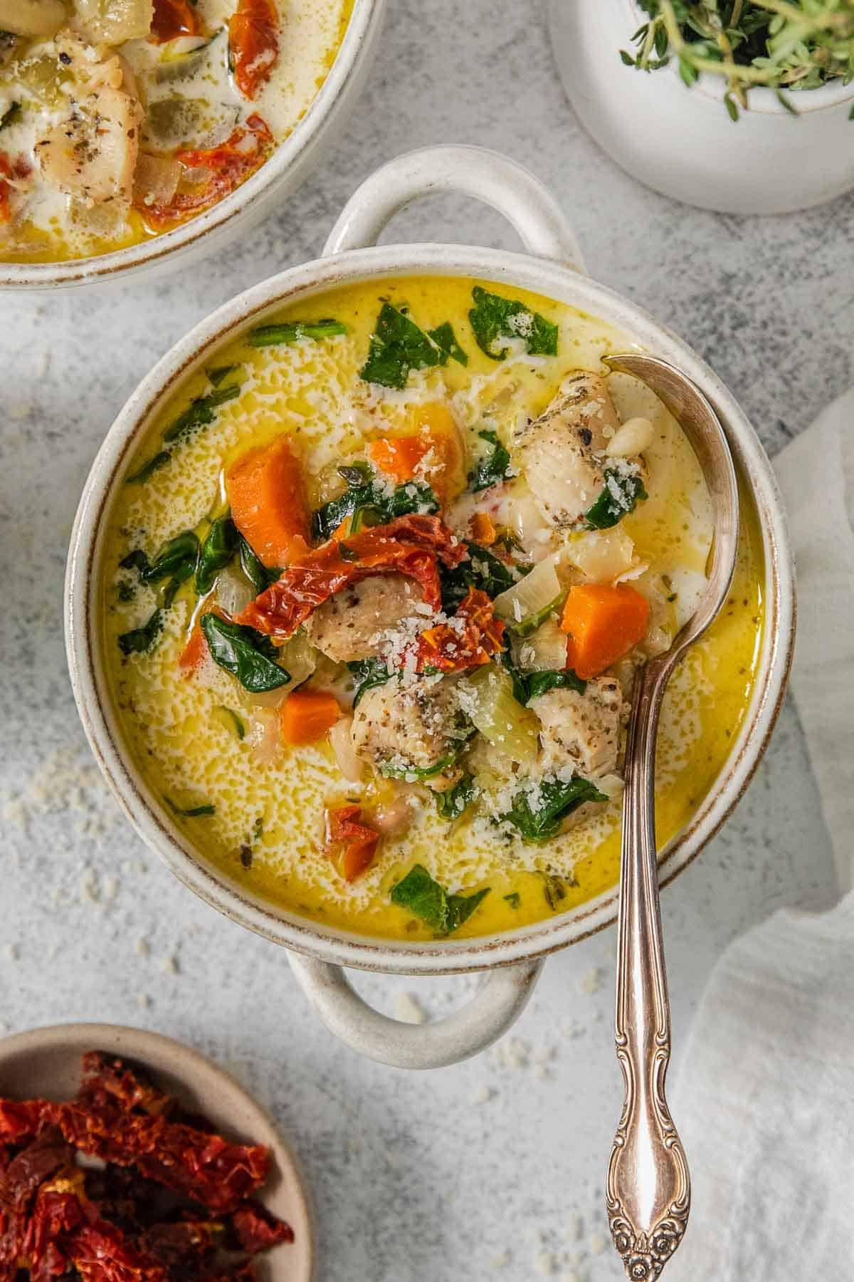 A bowl of easy tuscan chicken soup with carrots, spinach and sun dried tomatoes and a spoon.