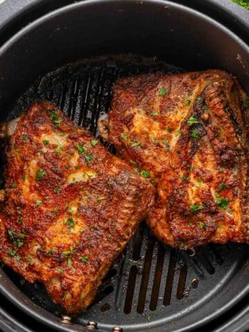 Two air fryer chicken thighs in an air fryer.