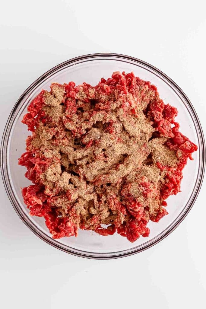 A bowl full of meat in a clear bowl topped with seasonings.