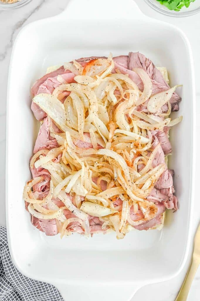 A baking dish filled with ham and onions on top of hawaiian rolls.