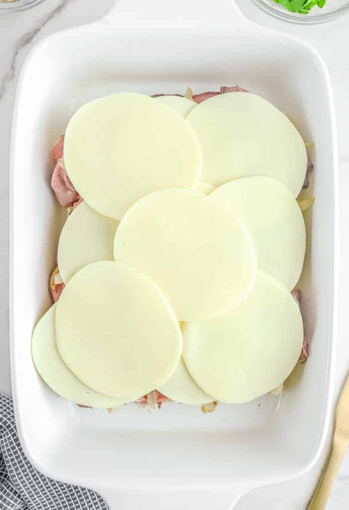 Provolone cheese added on top of ham in baking dish.