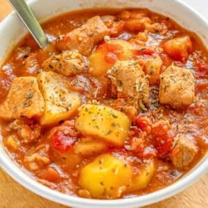 A bowl of pork stew in a white bowl with a silver spoon.