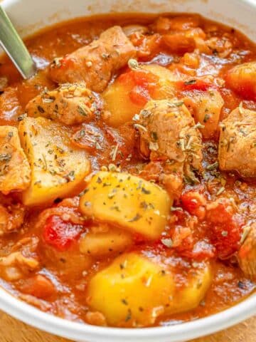 A bowl of pork stew in a white bowl with a silver spoon.