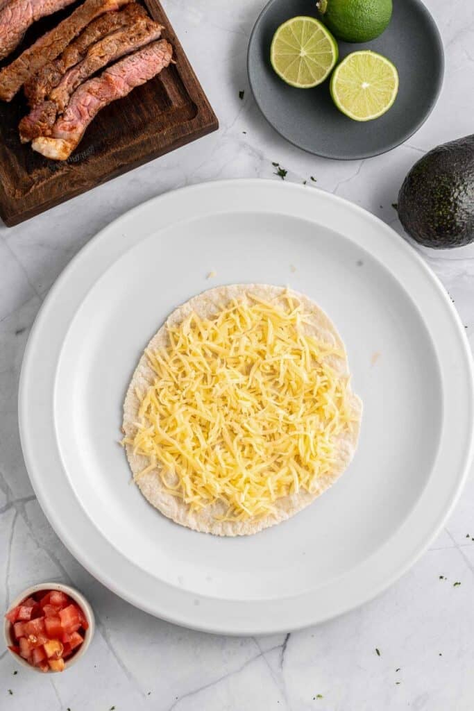 A white plate with a tortilla topped with cheese on it.