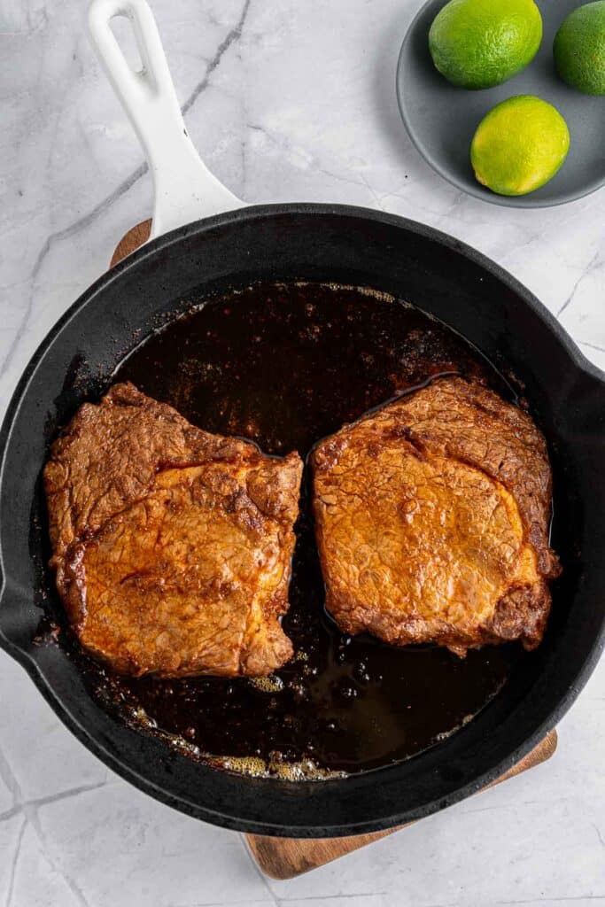 Two cooked steaks in a skillet on top of a wooden board.