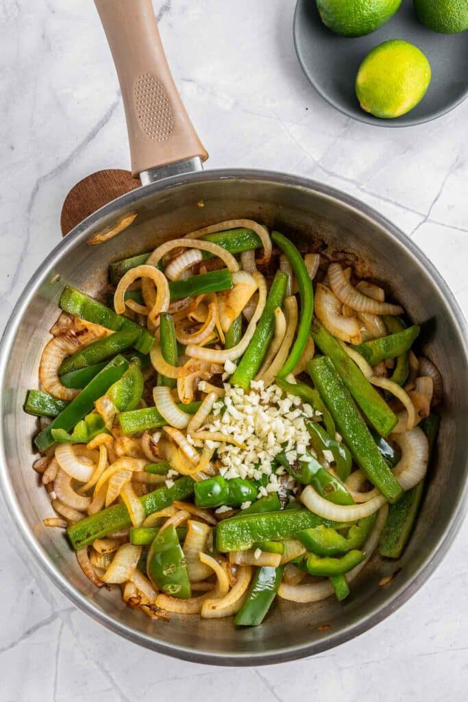 A pan with onions, green pepper and chopped garlic in it.