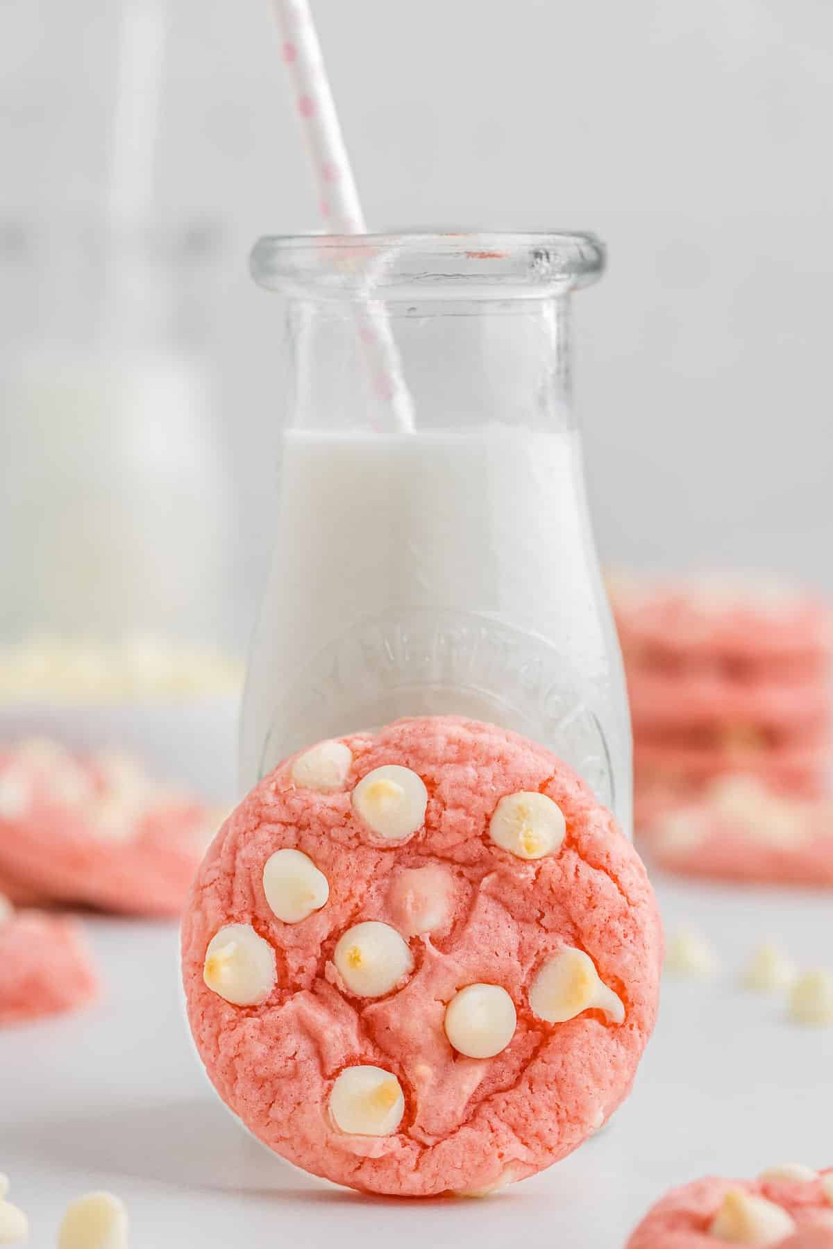 A strawberry cookie leaded up next to a glass of milk.