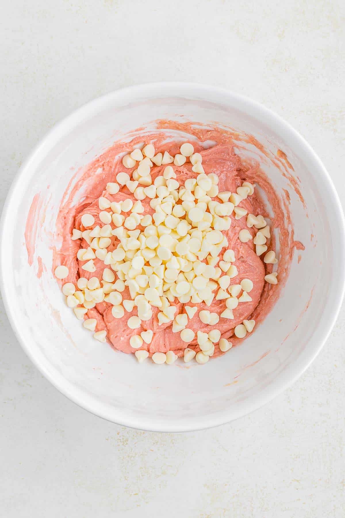A white bowl filled with strawberry cake mix and white chocolate chips.