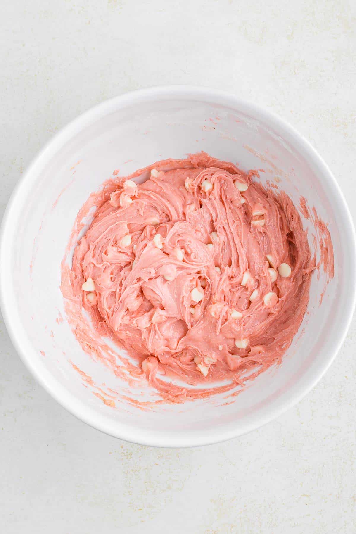 Strawberry cake mix with white chocolate ships in a white mixing bowl.