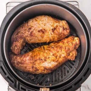 Golden brown pork tenderloins in an air fryer cooked to perfection topped with herbs.