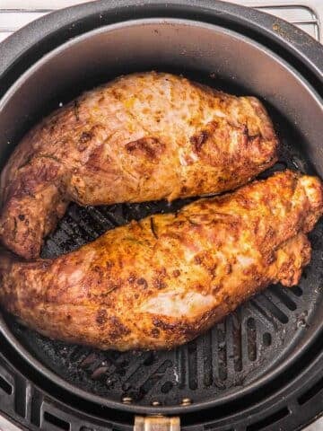 Golden brown pork tenderloins in an air fryer cooked to perfection topped with herbs.