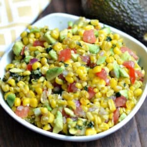 Corn salsa with avocado, red onion and tomato in a white bowl.