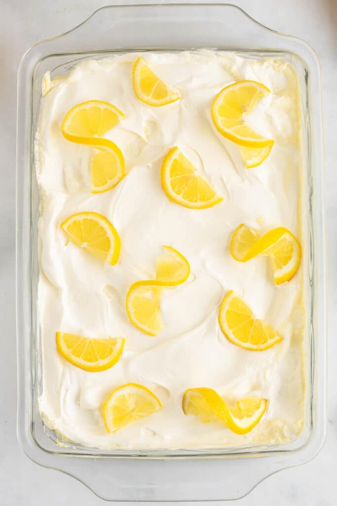 A glass baking dish filled with lemon icebox cake with lemon slice garnishes spread overtop.