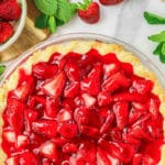 A strawberry pie in a glass pie dish next to a bowl of strawberries.