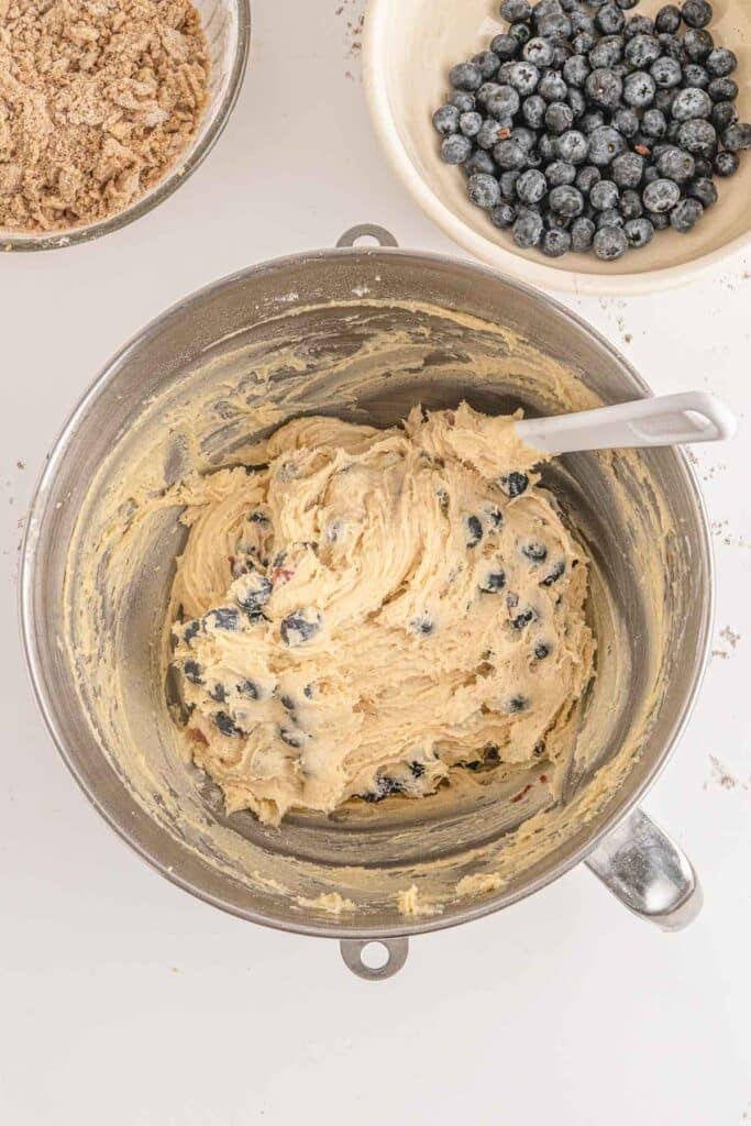 A bowl with freshly mixed blueberry buckle batter with a spoon inside, ready for baking.
