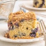 A slice of blueberry buckle on a white plate with a fork on the side.