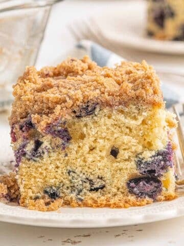 A slice of blueberry buckle on a white plate with a fork on the side.