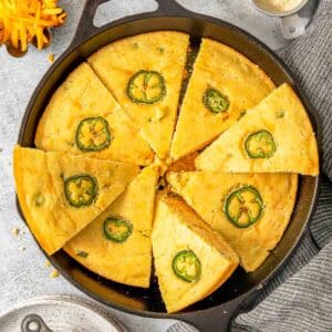 A skillet of sliced jalapeño cheddar cornbread topped with jalapeño.