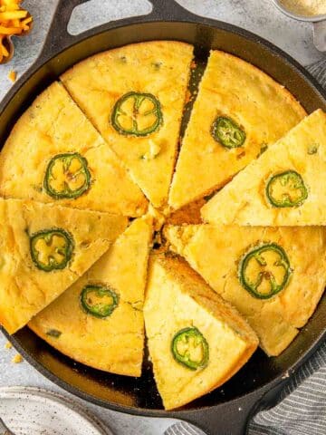 A skillet of sliced jalapeño cheddar cornbread topped with jalapeño.