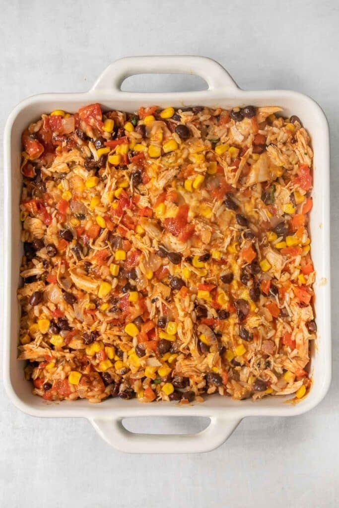 A baking dish filled with a chicken casserole with rice, tomatoes, black bean and corn.