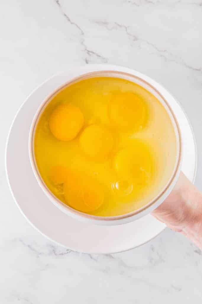 A person holding a clear glass bowl containing raw eggs.
