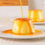 Caramel sauce being poured over top of Mexican flan on a white plate.