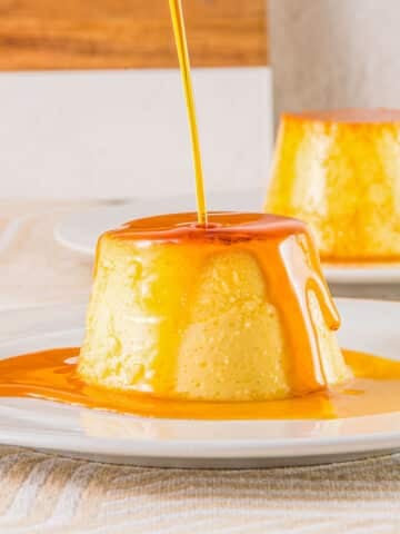 Caramel sauce being poured over top of Mexican flan on a white plate.
