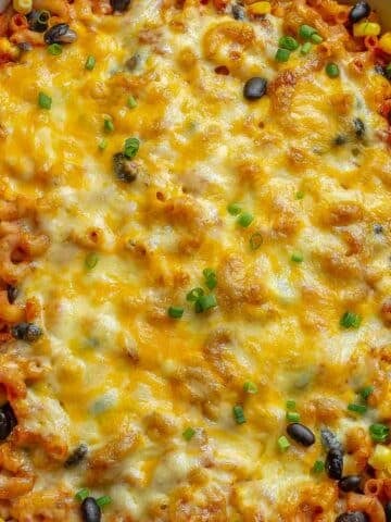 A freshly baked mexican mac and cheese in a large red casserole dish topped with scallions ready to serve.