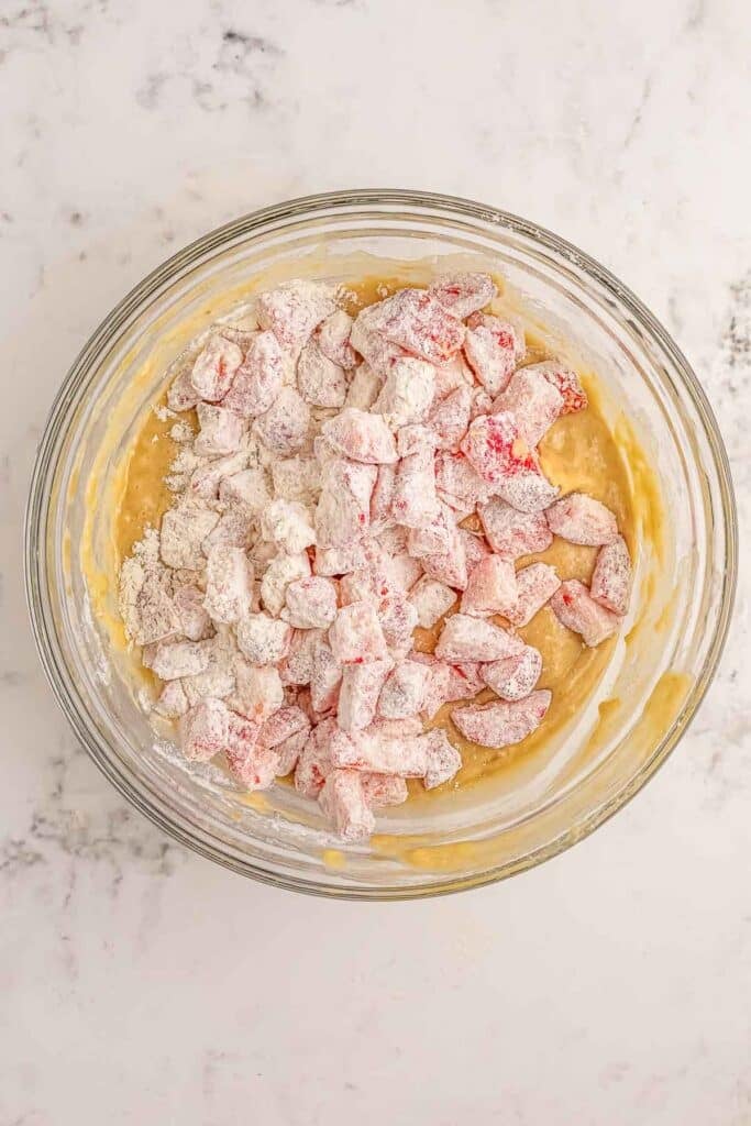A glass bowl containing batter mixed with strawberry chunks.