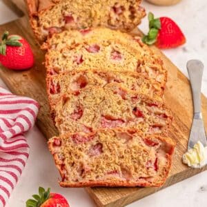 A freshly baked strawberry banana bread loaf, sliced on a wooden board.