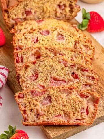 A freshly baked strawberry banana bread loaf, sliced on a wooden board.