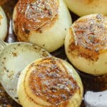 Close-up of balsamic roasted onions with browning and caramelization, sprinkled with seasonings, in a baking dish.