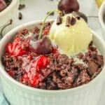 Cherry dump cake in a white bowl topped with ice cream and chocolate curls garnished with a cherry.