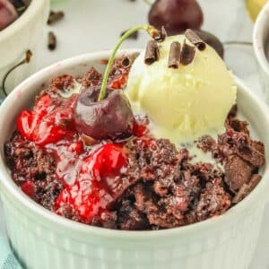 Cherry dump cake in a white bowl topped with ice cream and chocolate curls garnished with a cherry.