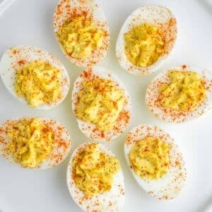 Several deviled eggs garnished with paprika arranged on a white plate.