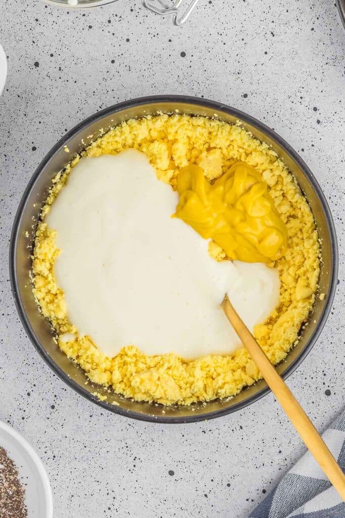 A mixing bowl of crumbled hard boiled egg with mayonnaise and mustard added in.